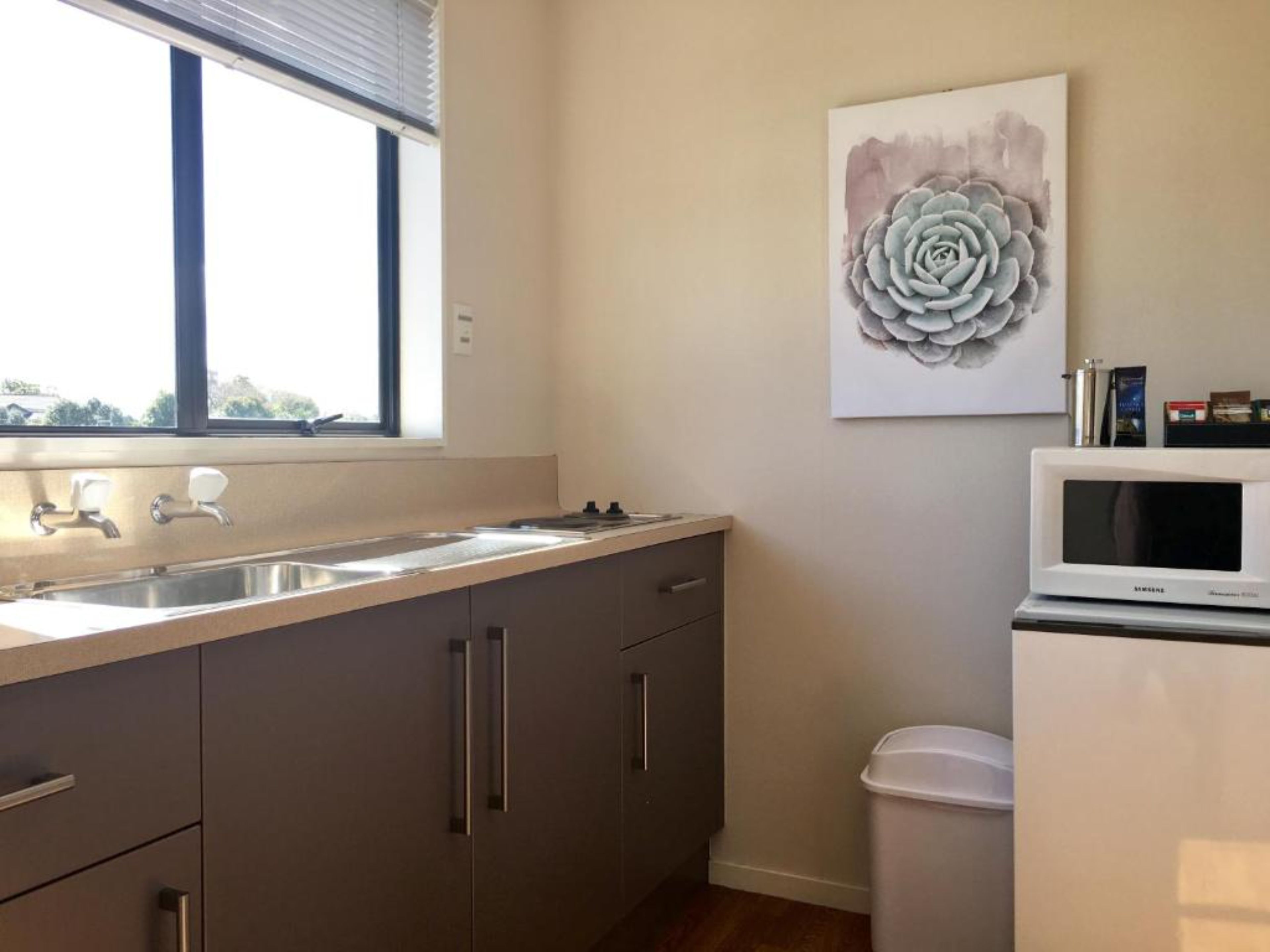 A modern kitchen with a stainless steel sink, grey cabinets, a white microwave, and a window with blinds.