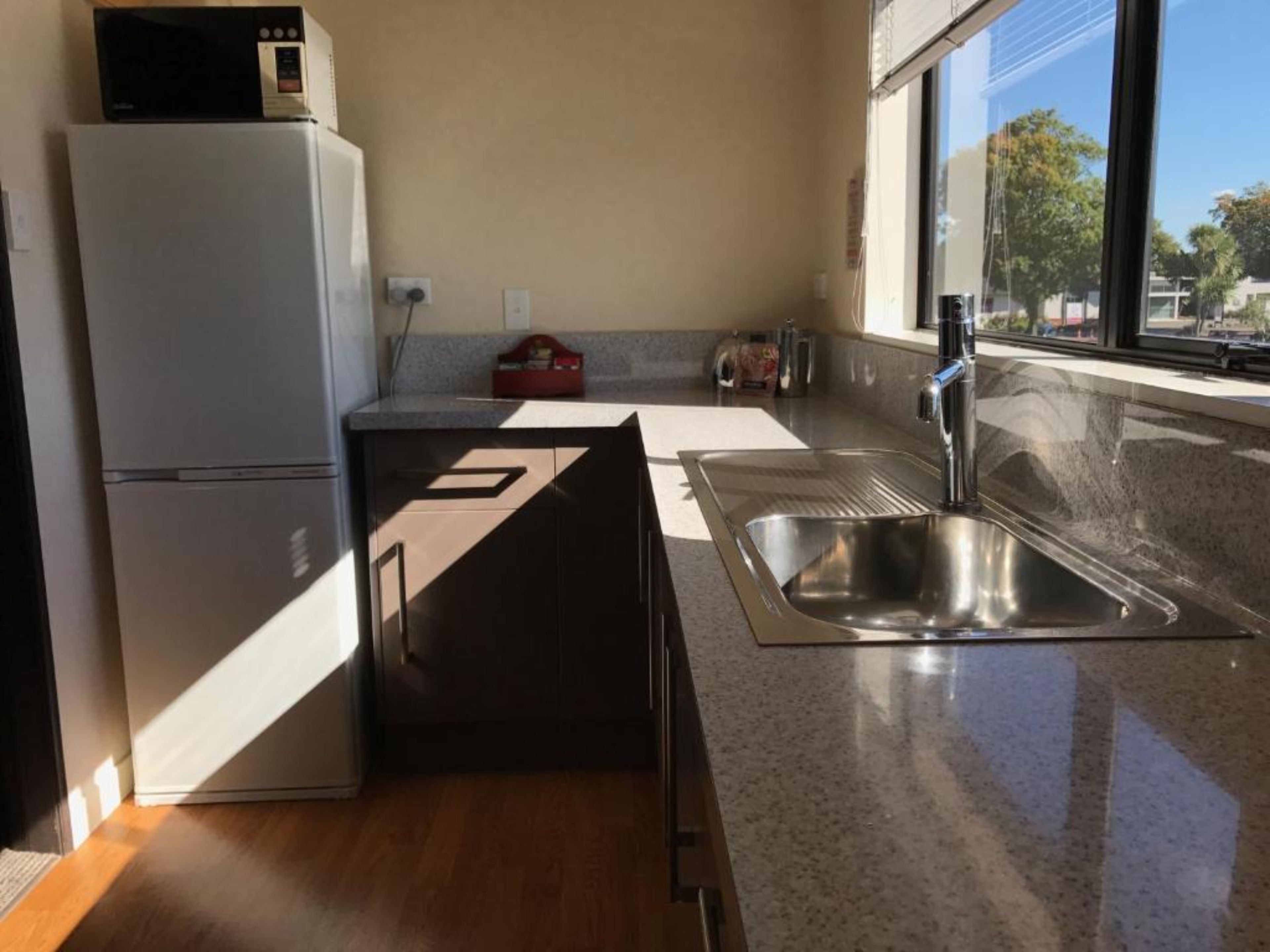 Kompakti keittiö, jossa on jääkaappi, pesuallas ja ikkuna, josta tulee luonnonvaloa.