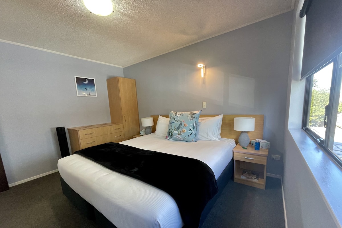Habitación de hotel con cama, mesitas de noche, una ventana y una lámpara de pared.
