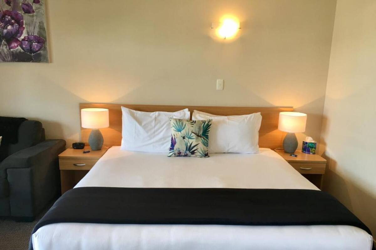Habitación de hotel con una cama grande, dos mesitas de noche con lámparas, un pequeño escritorio y un sofá, además de un cuadro en la pared.