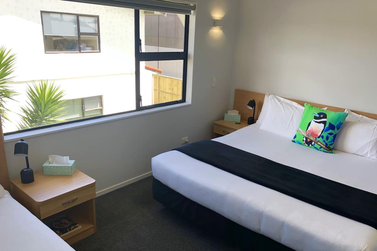 Una habitación de hotel con cama, mesitas de noche, una lámpara y ventana con vistas al exterior.