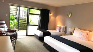 Une chambre d’hôtel avec deux lits, une chaise, une table et une vue sur la verdure par la porte.