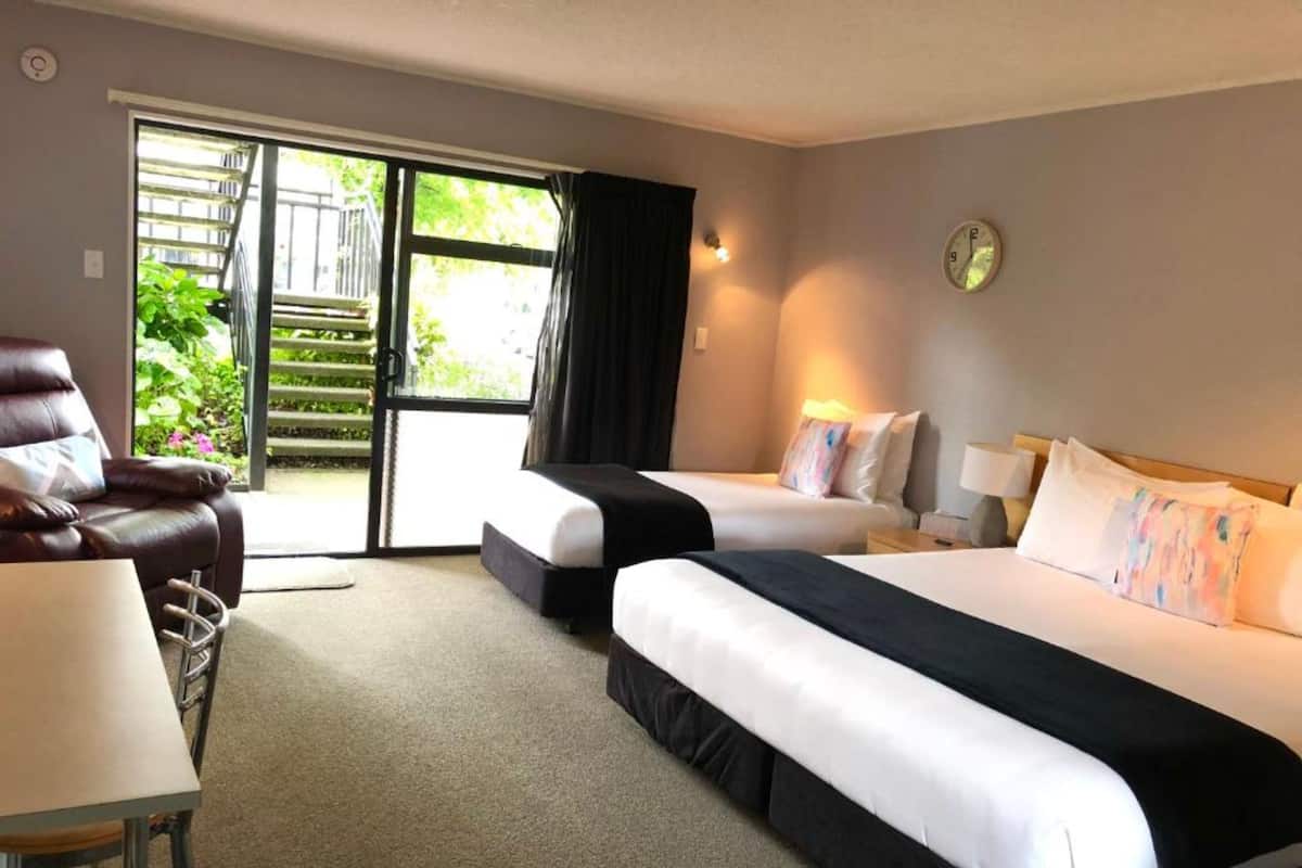 Habitación de hotel con dos camas, una silla, una mesa y vistas a zonas verdes a través de la puerta.