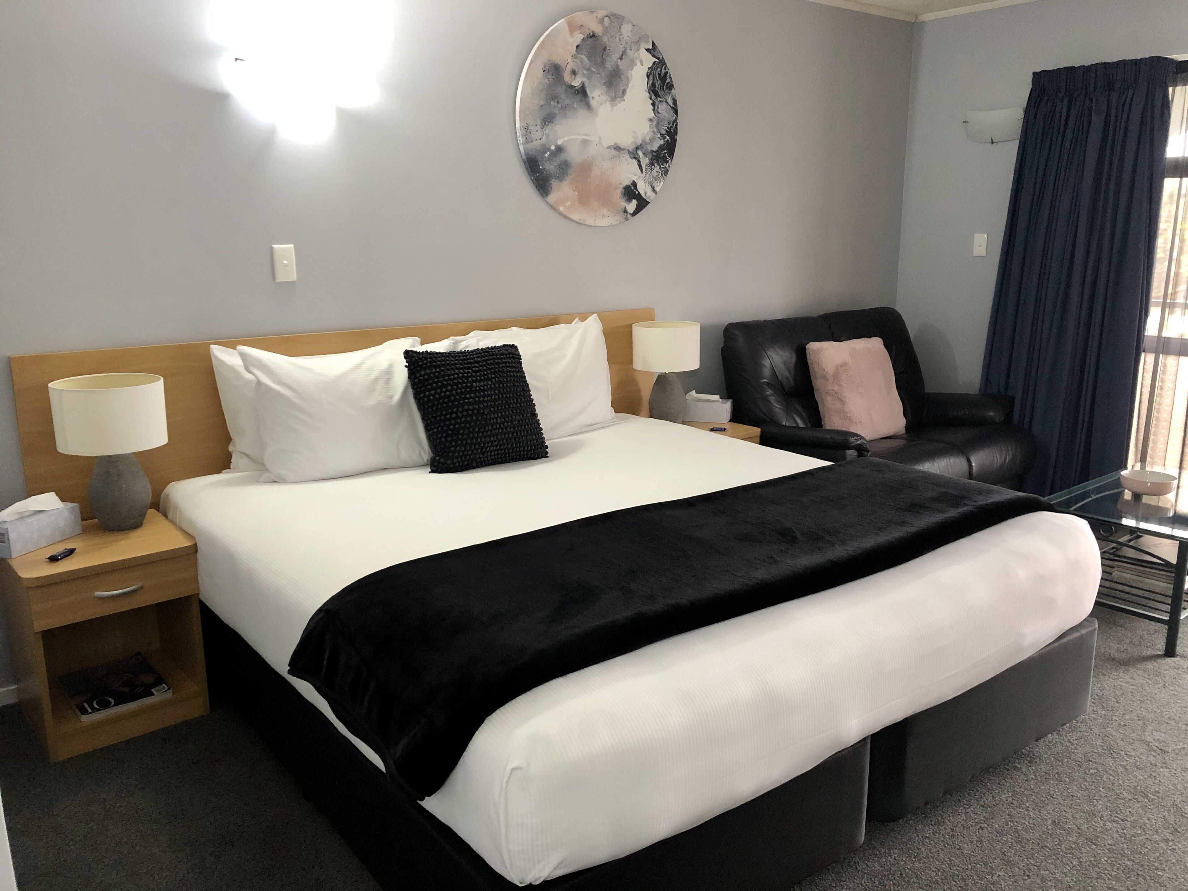 A hotel room with a large bed, a desk, a chair, a lamp, and a wall art piece.
