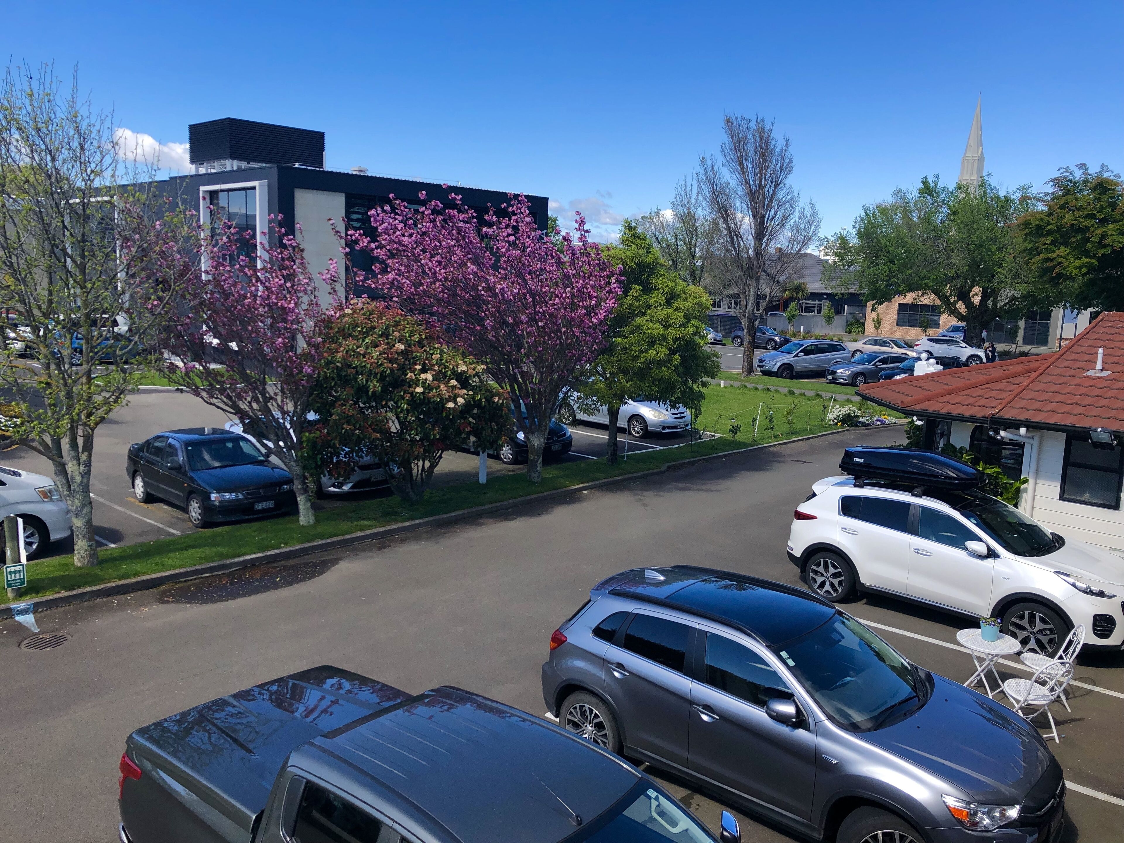 Ein Parkplatz mit mehreren Autos, ein modernes Gebäude und ein Kirchturm im Hintergrund.