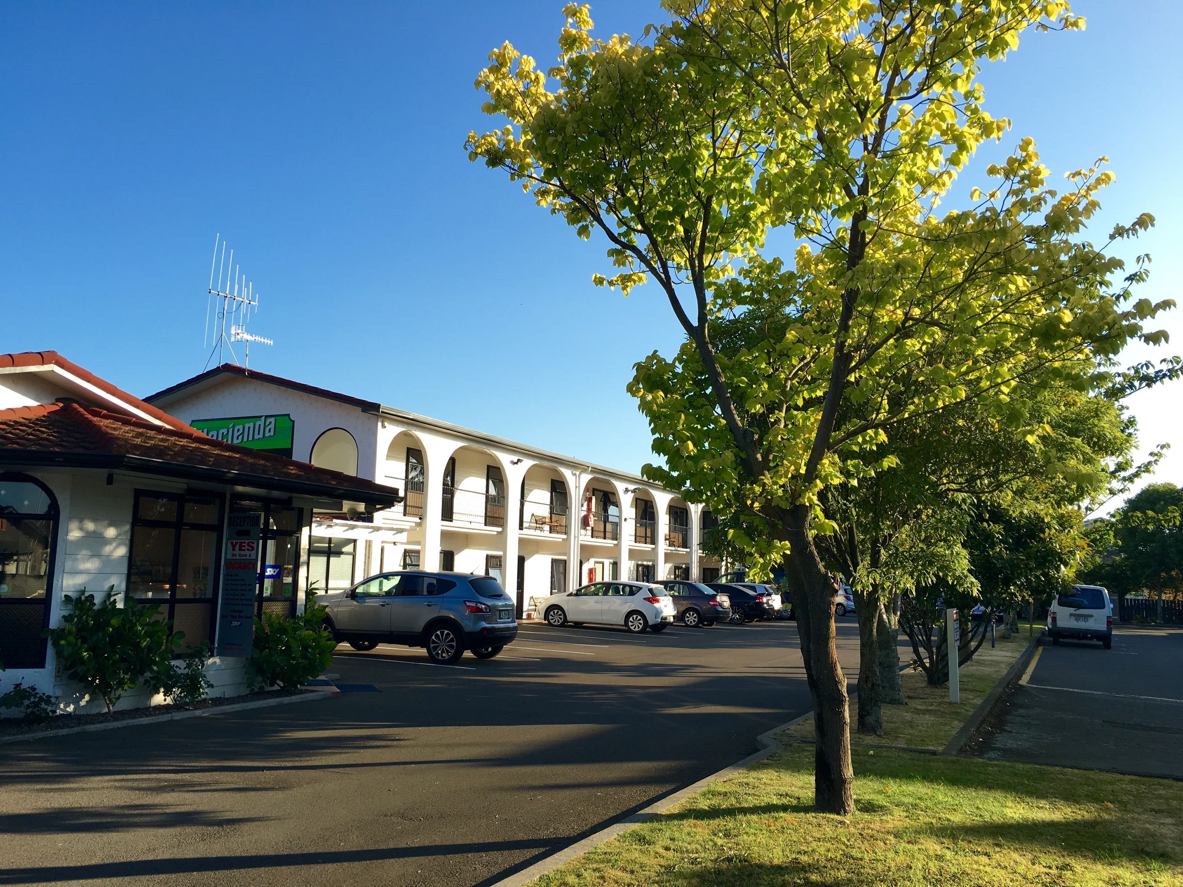 A building with a white facade and arched windows, a sign reading "Acacia," and parked cars along the street.