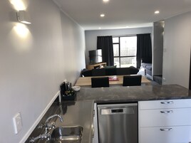 Una cocina moderna con lavavajillas integrado, una zona de comedor con mesa y sillas de madera, un sofá y un televisor al fondo.