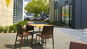 Un espace extérieur aménagé avec une table et des chaises, une enseigne indiquant qu'il s'agit d'un café, et un bâtiment moderne en arrière-plan.