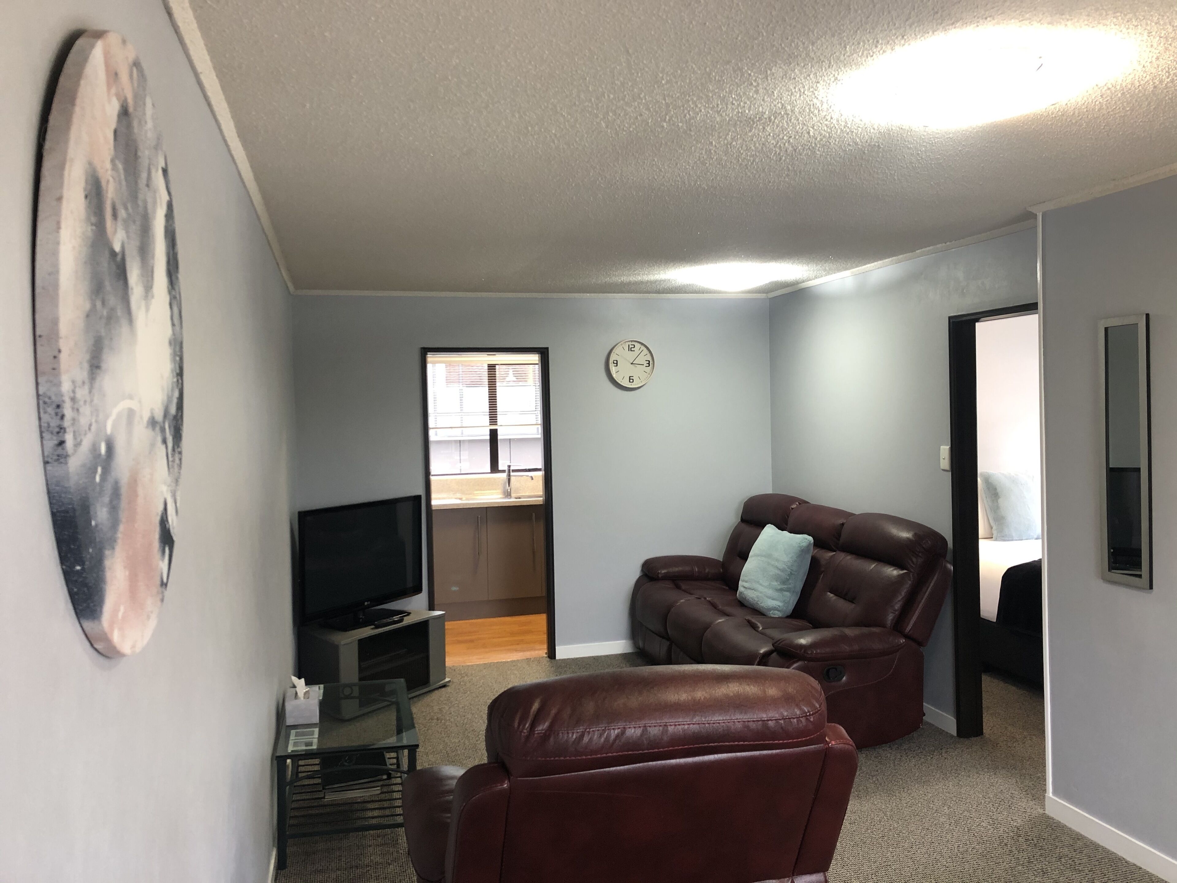 A living room with a TV, leather recliner, and a clock on the wall.
