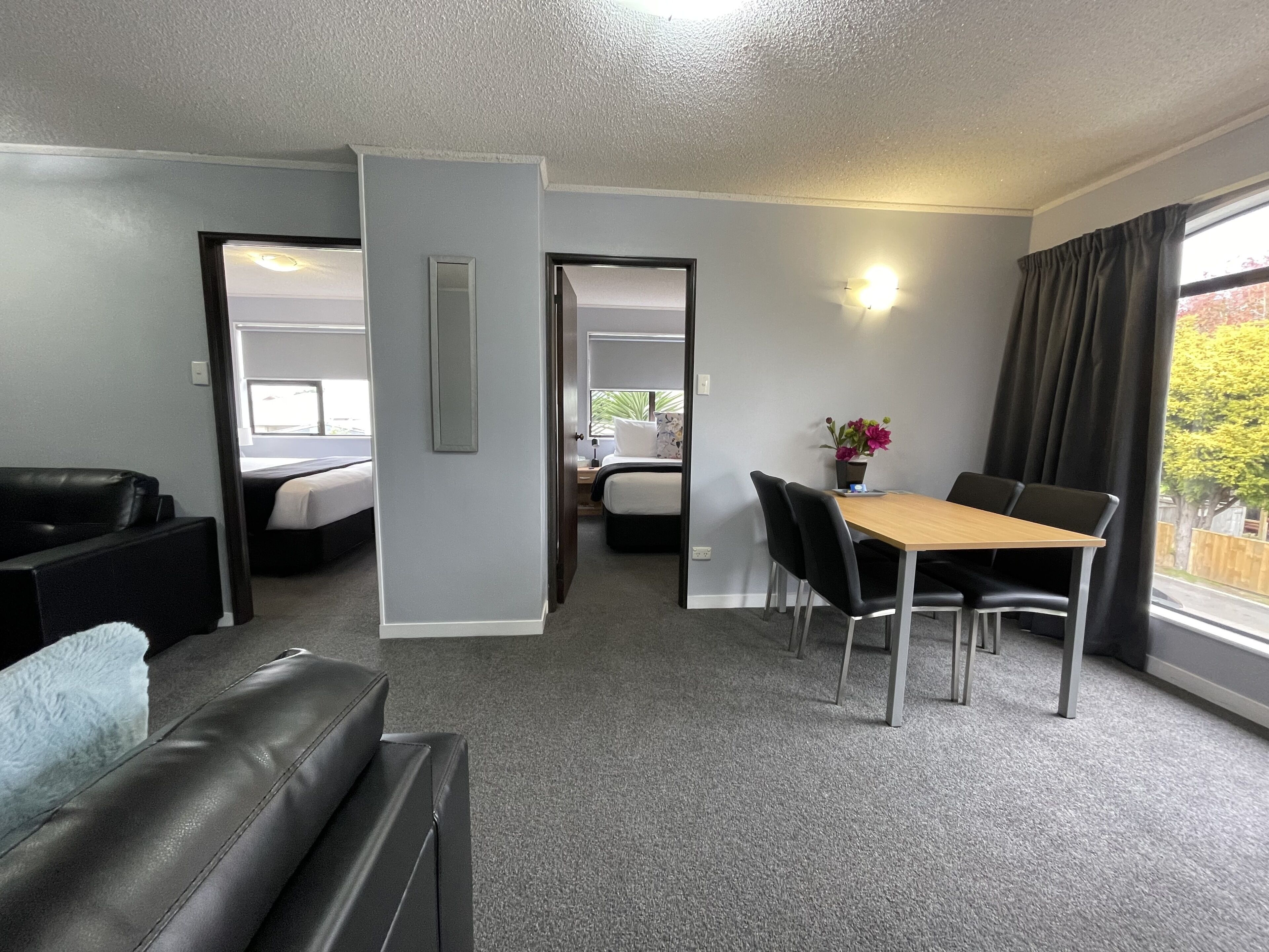 Una habitación de hotel con cama, zona de estar con sofá, mesa de comedor con sillas y ventana con cortinas.
