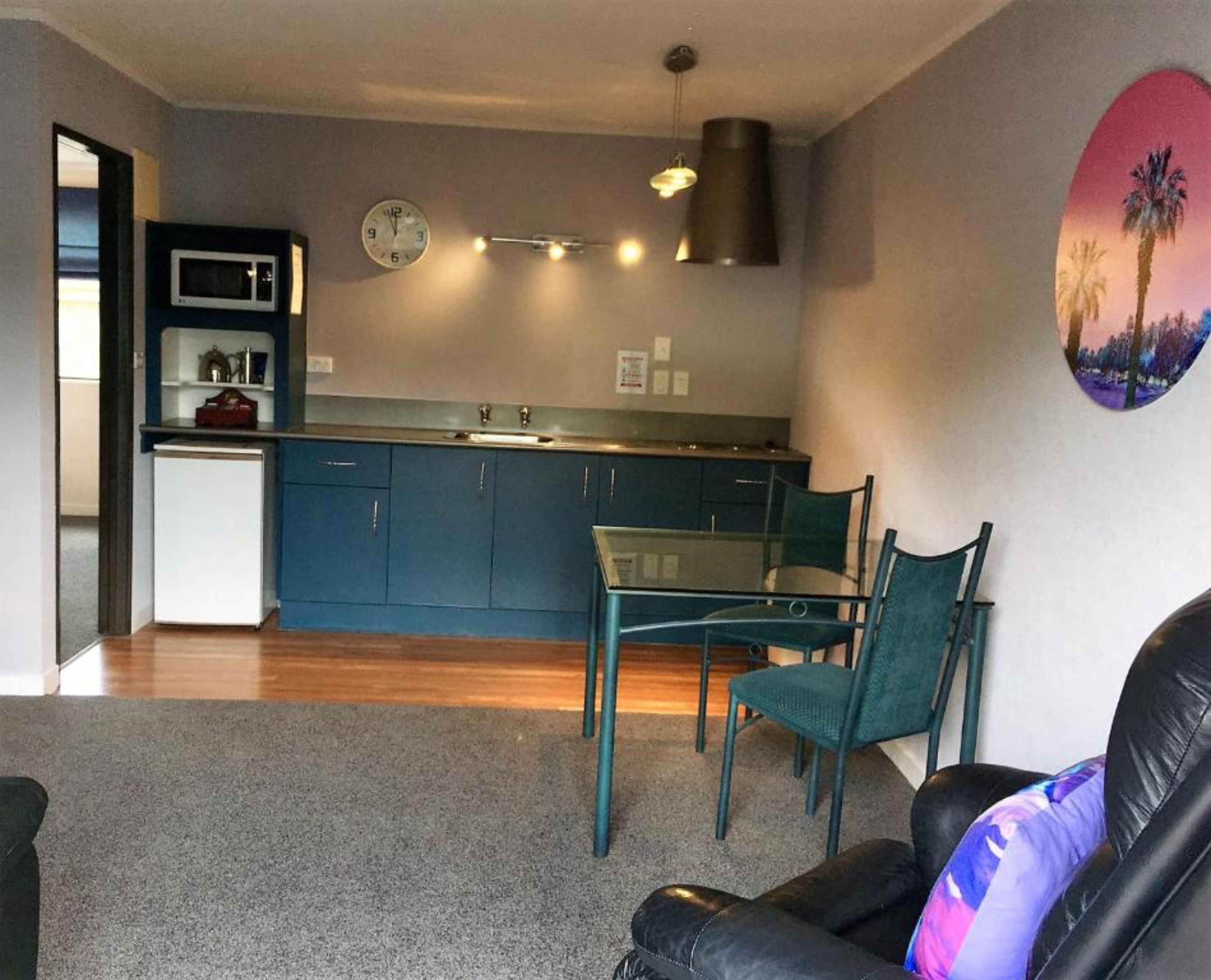 A compact living space with a kitchenette, a dining area with a glass table and chairs, and a living room with a leather sofa.