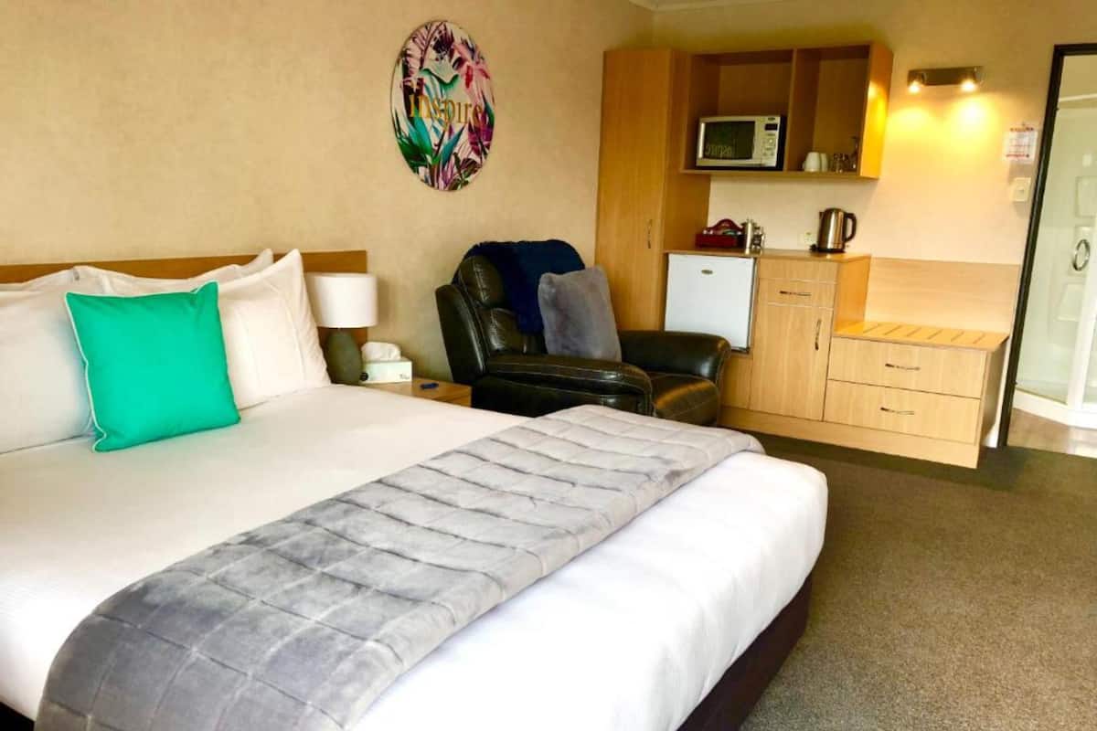 Una habitación de hotel con una cama grande, una silla, un escritorio y un microondas.