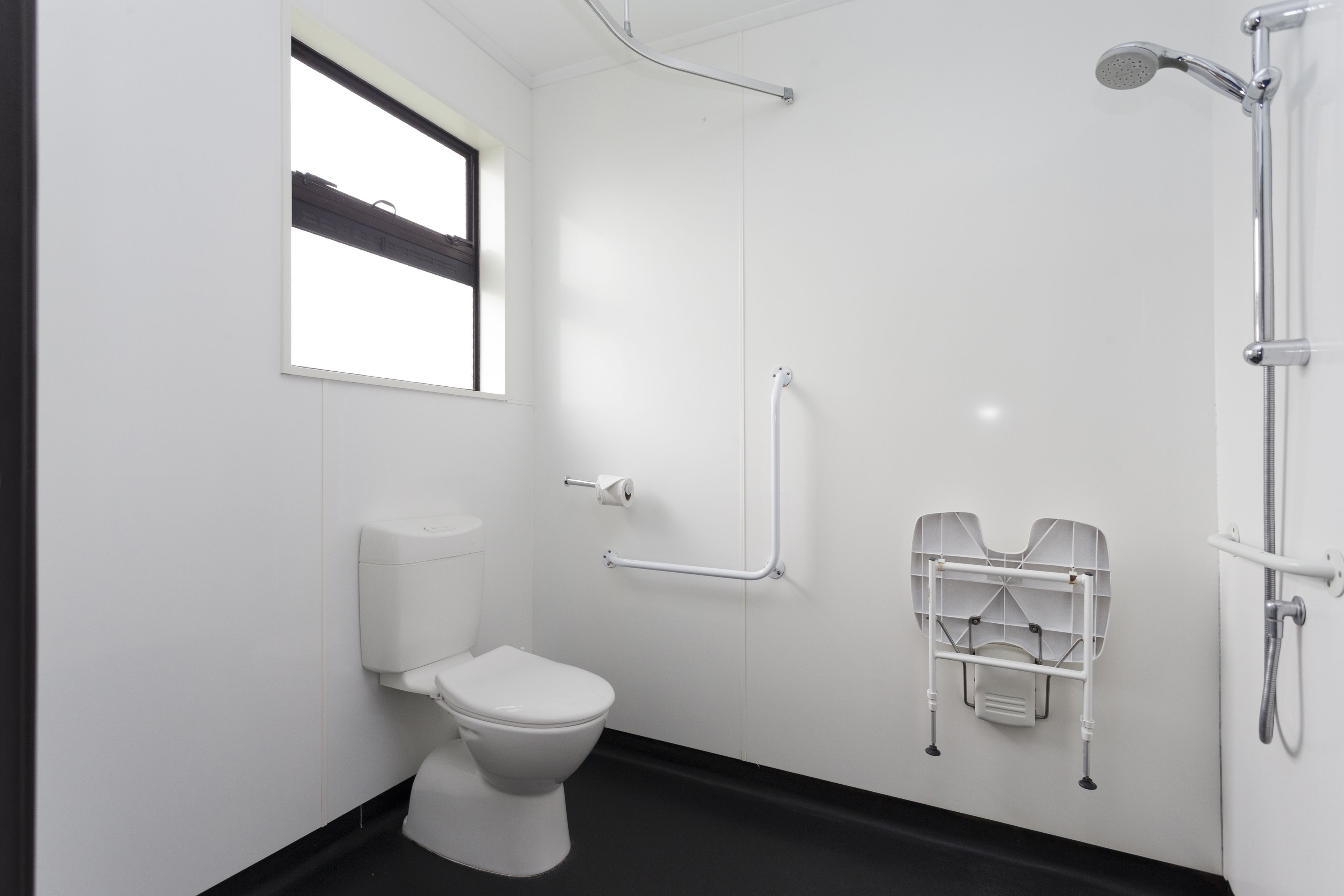 A modern bathroom with a toilet, a shower, and a handrail.