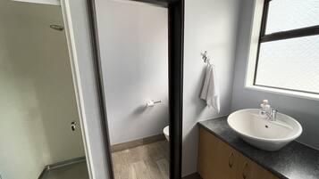 Uma casa de banho com uma pia branca, uma toalha pendurada na parede e uma porta de chuveiro.
