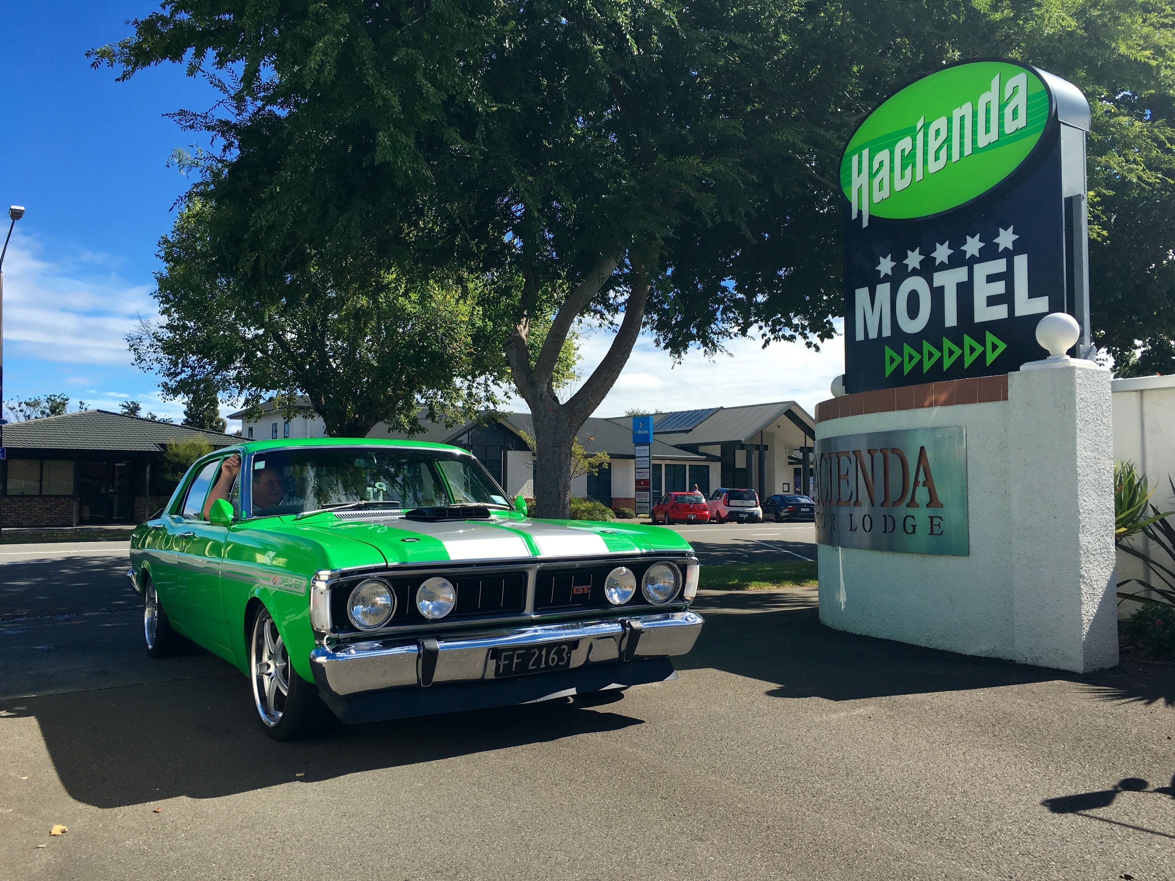 A vintage green and white car parked in front of a motel sign.