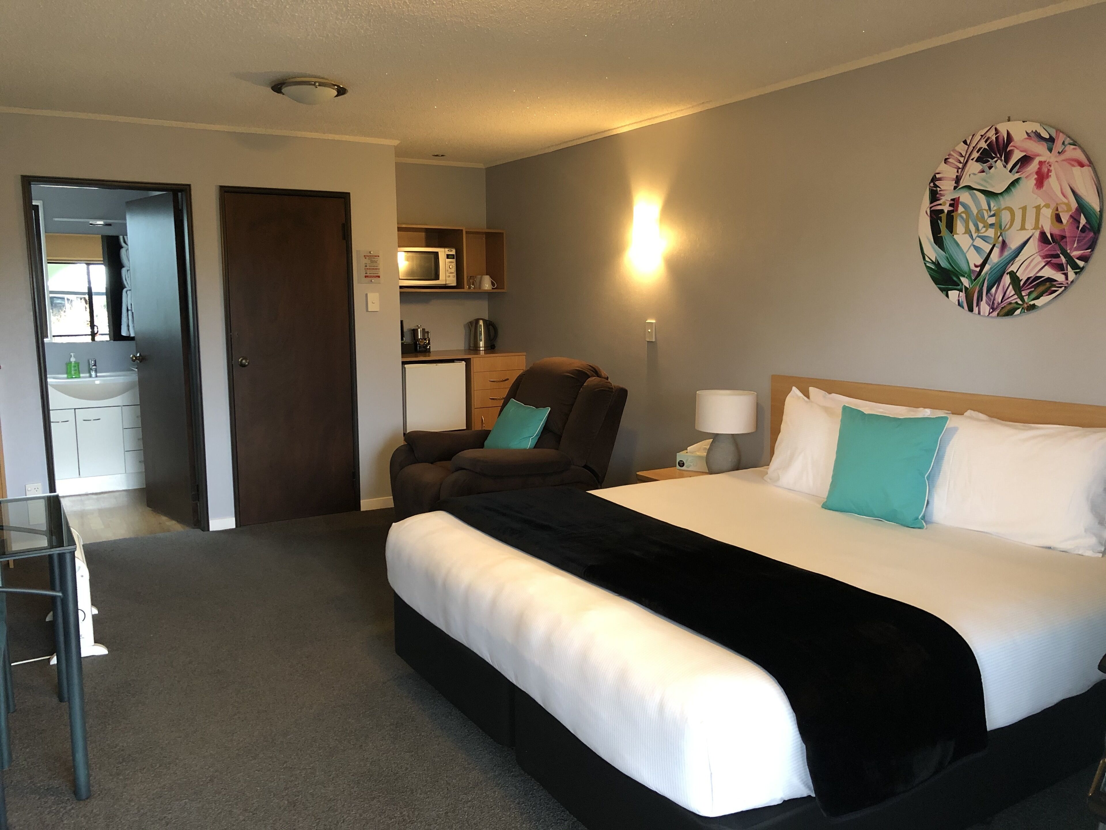 A hotel room with a bed, a chair, a desk, a microwave, and a small kitchenette.