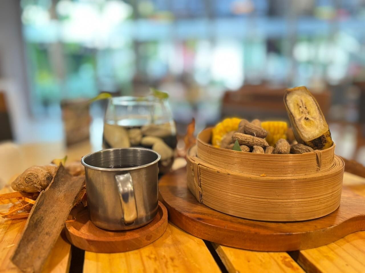 Una mesa de madera con una taza de metal, un vaporera de bambú y un tarro de especias.