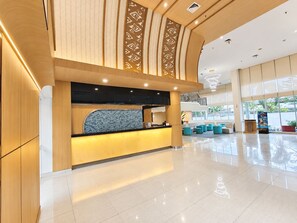 A modern hotel lobby with a reception desk, seating area, and large windows. - Metland Hotel Cirebon (North Cirebon)