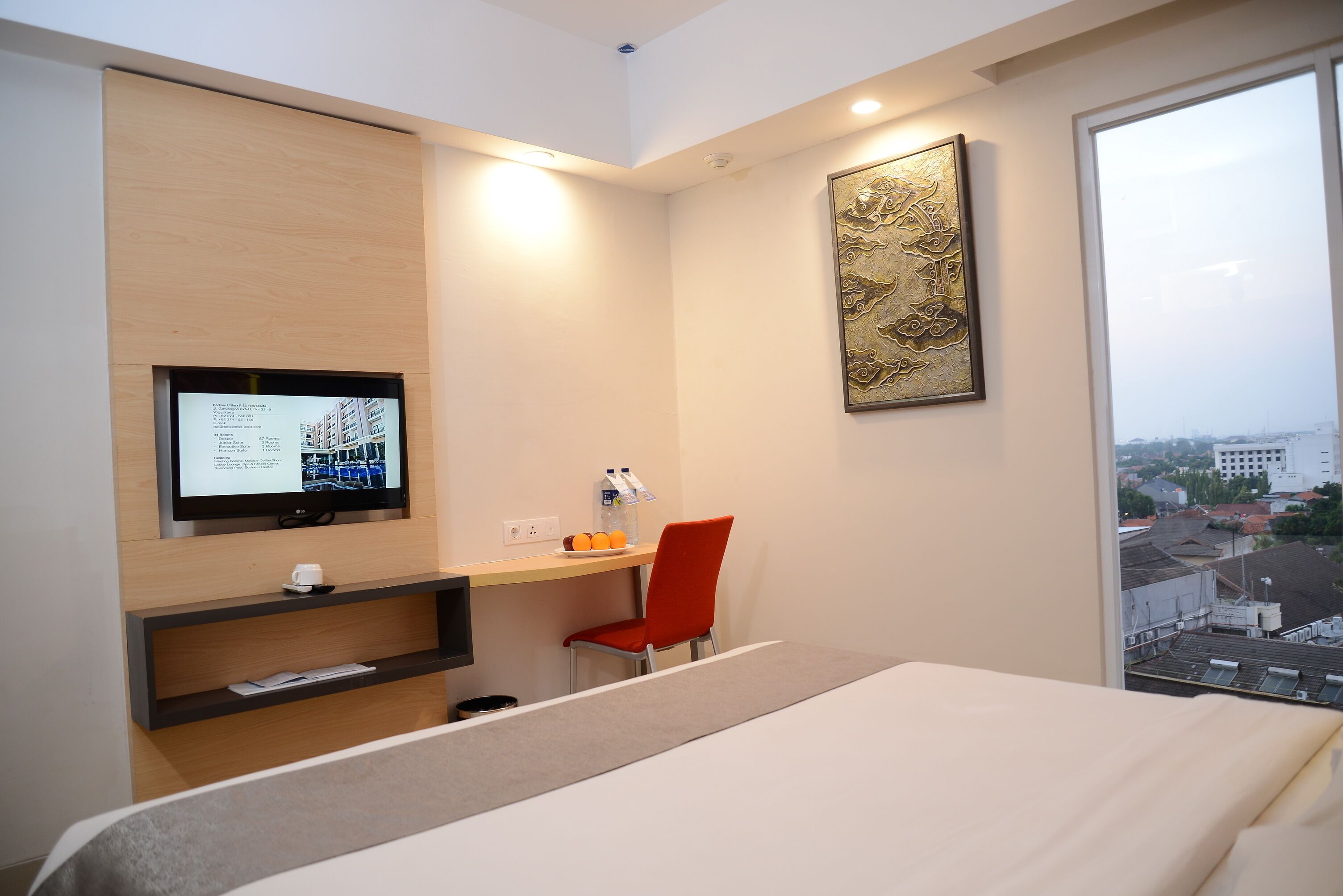Habitación de hotel con cama, escritorio con computadora, silla, televisor y ventana con vista a la ciudad.