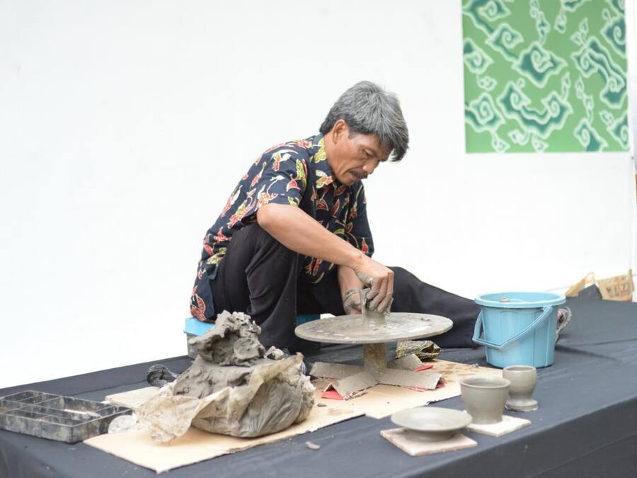 Una persona trabajando en cerámica sobre una mesa con un cubo azul, un torno de alfarería y diversas piezas de cerámica.