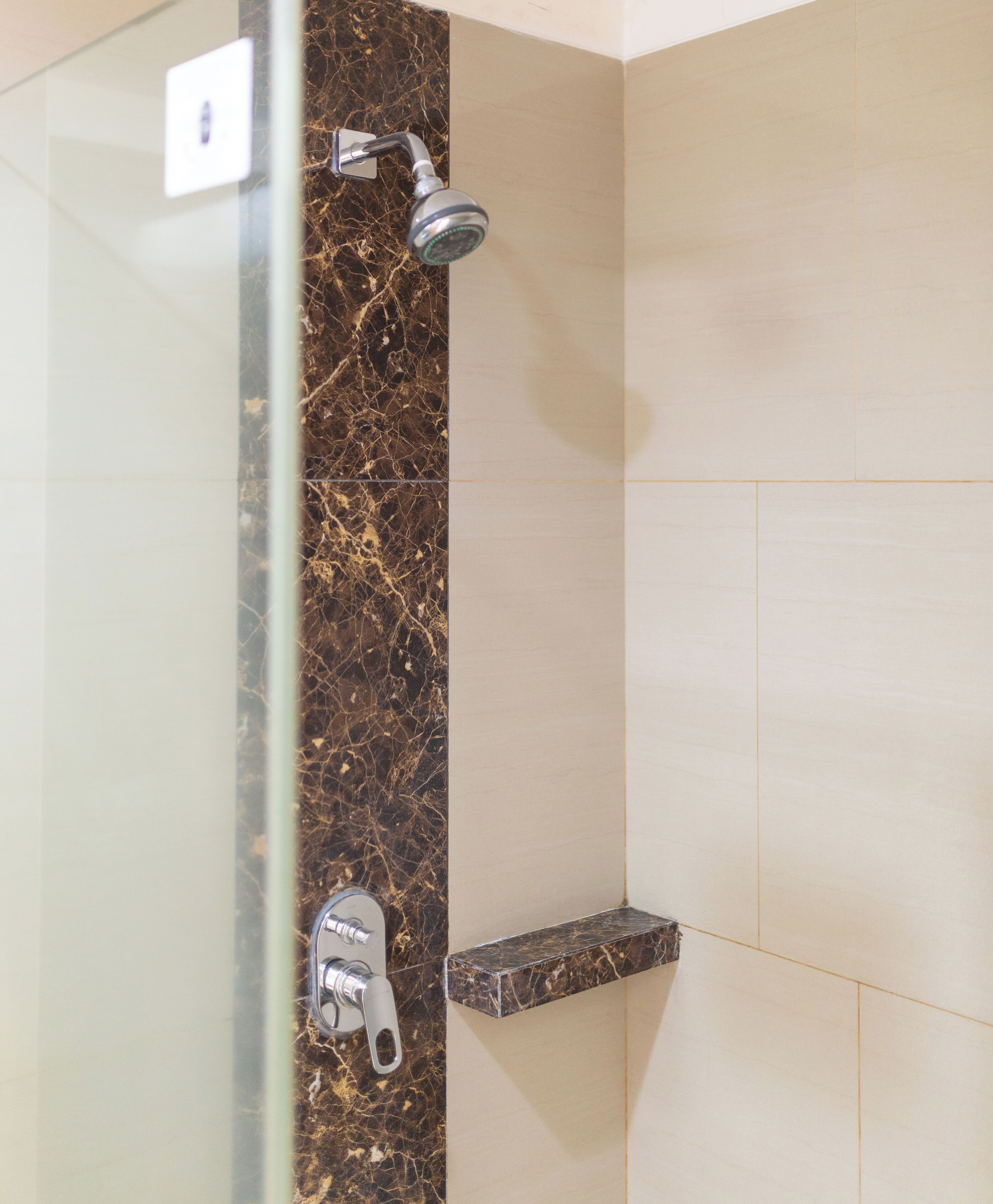 A bathroom with a glass shower enclosure, a marble wall, and a beige tiled shower area.