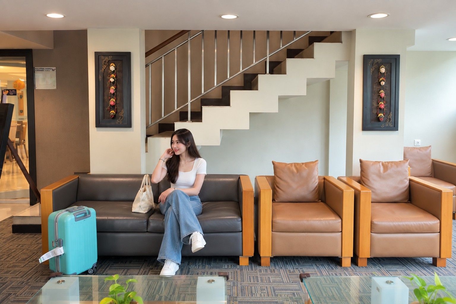 A hotel lobby with a staircase, a sofa, a chair, and a blue suitcase.