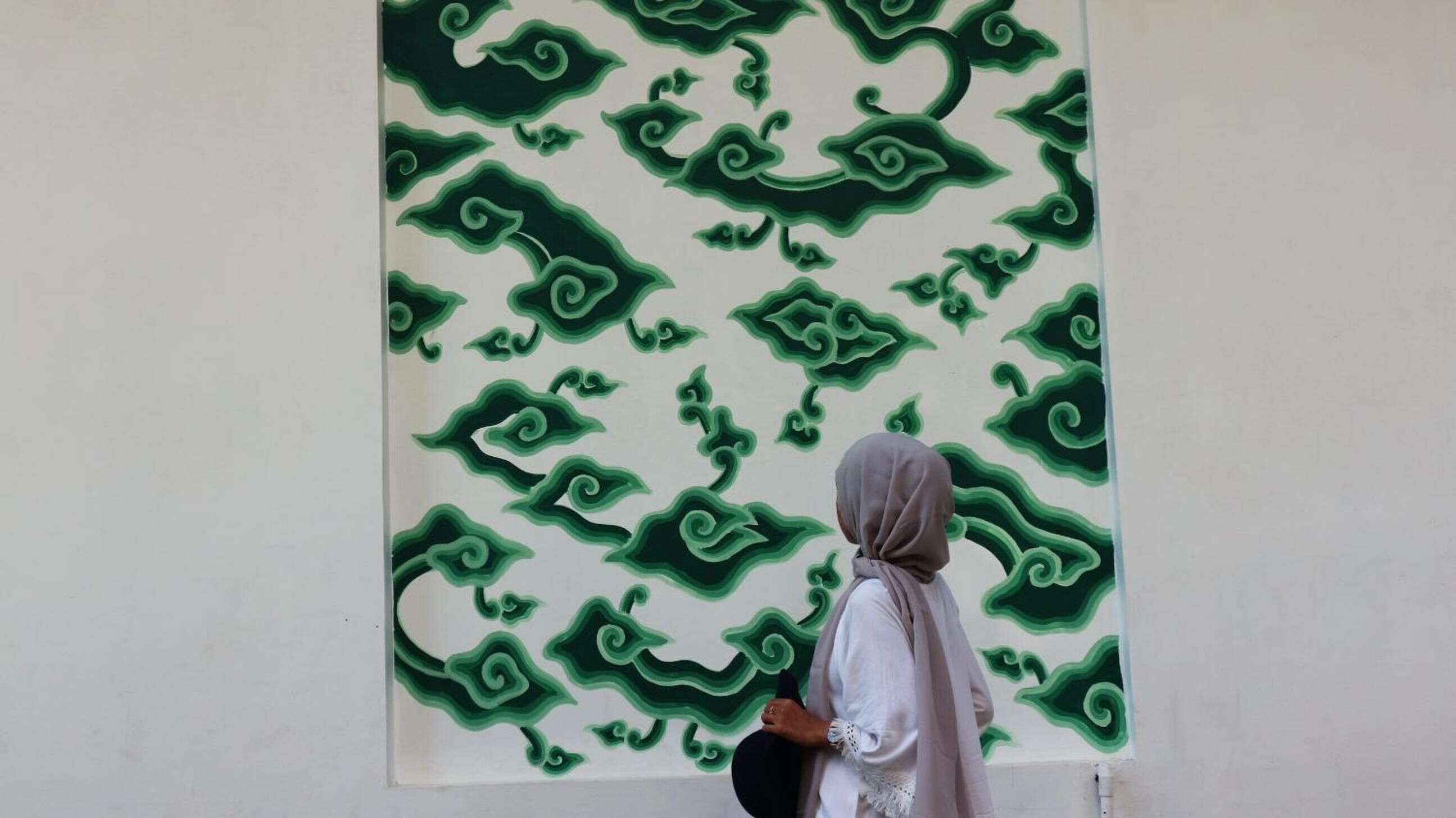 A person standing in front of a large wall with a green abstract pattern.