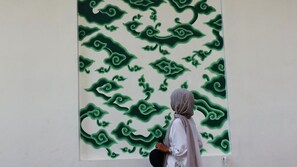A person standing in front of a large wall with a green abstract pattern.