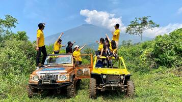 Um grupo de pessoas em um veículo todo-terreno amarelo em uma área gramada, com uma montanha ao fundo.