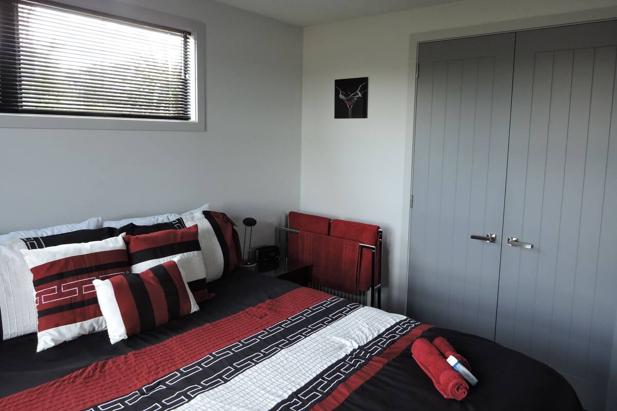 Un dormitorio con cama, ventana con persianas, puerta y una obra de arte colgada en la pared.