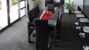 Una sala de conferencias moderna con una mesa de vidrio, sillas negras y un mantel individual rojo.