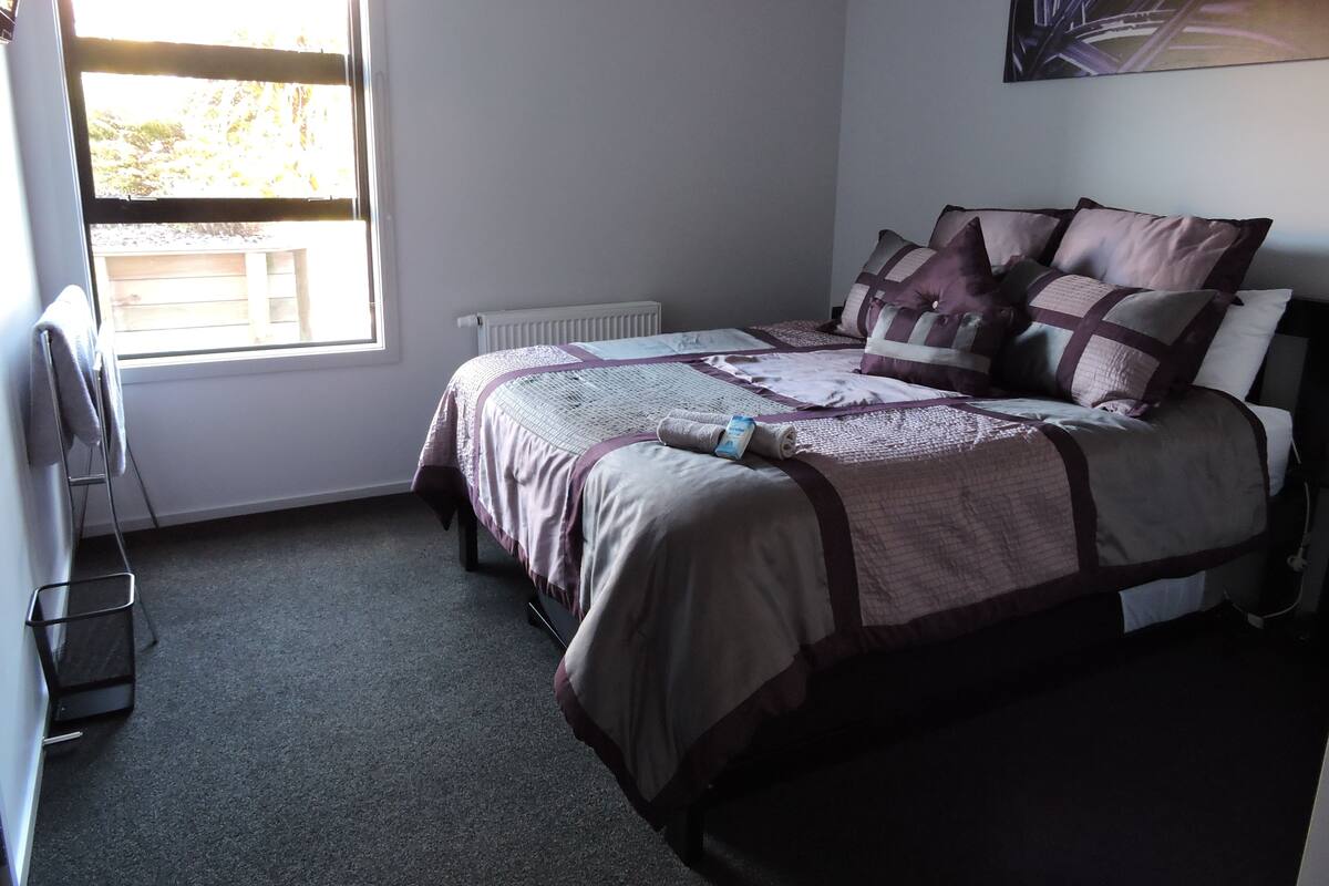 Un dormitorio con una cama, un radiador, una ventana y un cuadro en la pared.