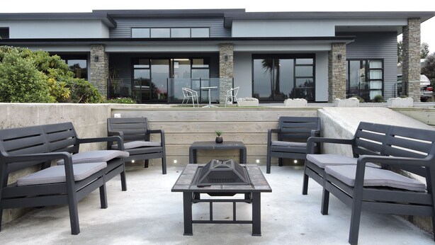 Un patio exterior con mobiliario moderno, incluyendo una mesa y sillas, frente a un edificio contemporáneo con ventanas amplias y detalles de piedra.