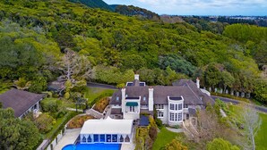 Uma casa grande com piscina, rodeada por vegetação exuberante e colinas.