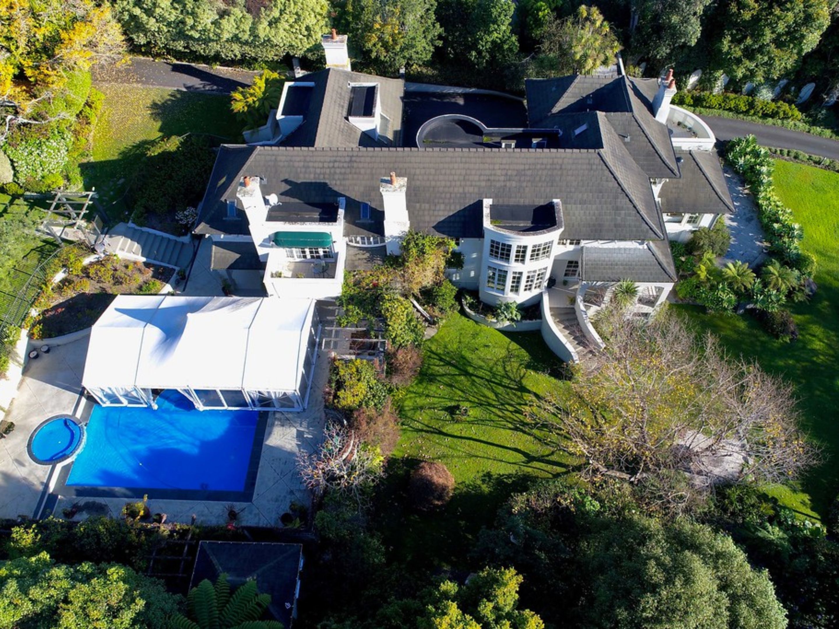 A large, modern house with a swimming pool, multiple chimneys, and a well-maintained garden.