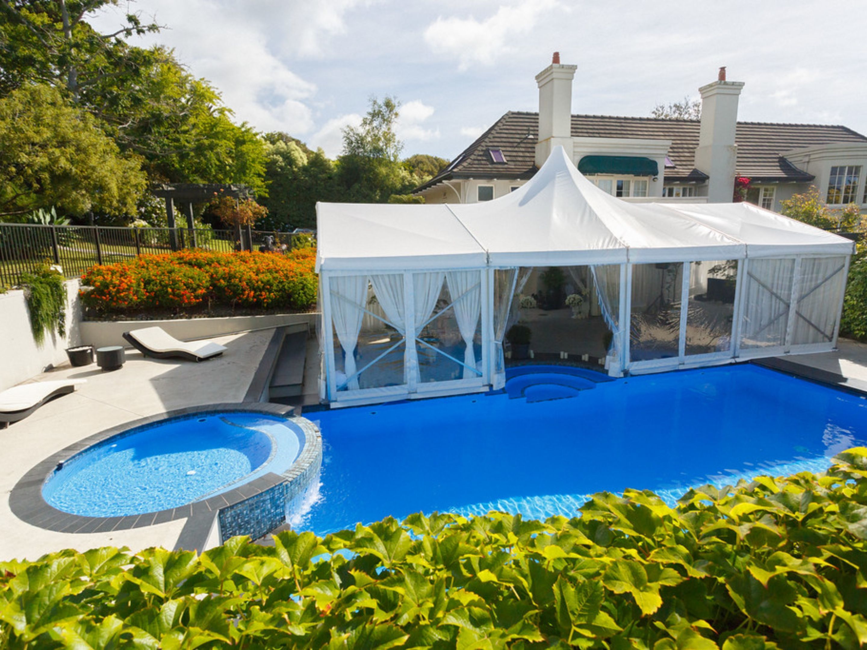 A swimming pool with a white tent structure, lounge chairs, and a house in the background.