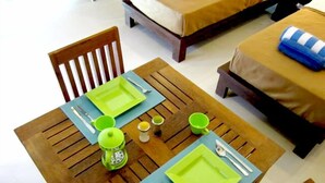 A dining table set with green plates, cutlery, and a green cup, with a bed and a blue-striped pillow in the background.