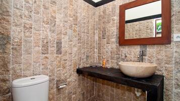 A bathroom with stone walls, a wooden-framed mirror, a black countertop, and a white toilet.