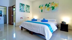 A hotel room with a large bed, white bedding, and blue accents. There are two wall-mounted paintings of tropical flowers.