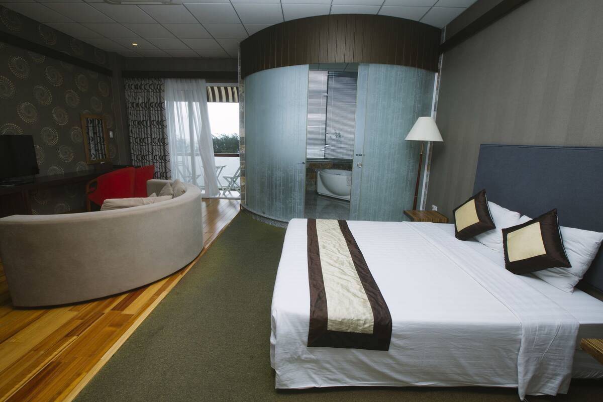 Ein Hotelzimmer mit einem großen Bett, einer gebogenen Sitzecke, einem Fernseher und Blick ins Freie.
