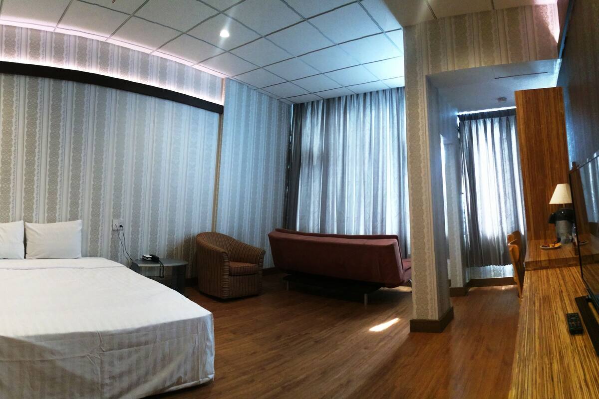 Ein Hotelzimmer mit einem großen Bett, einer kleinen Couch, einem Holztisch und einem Fernseher.