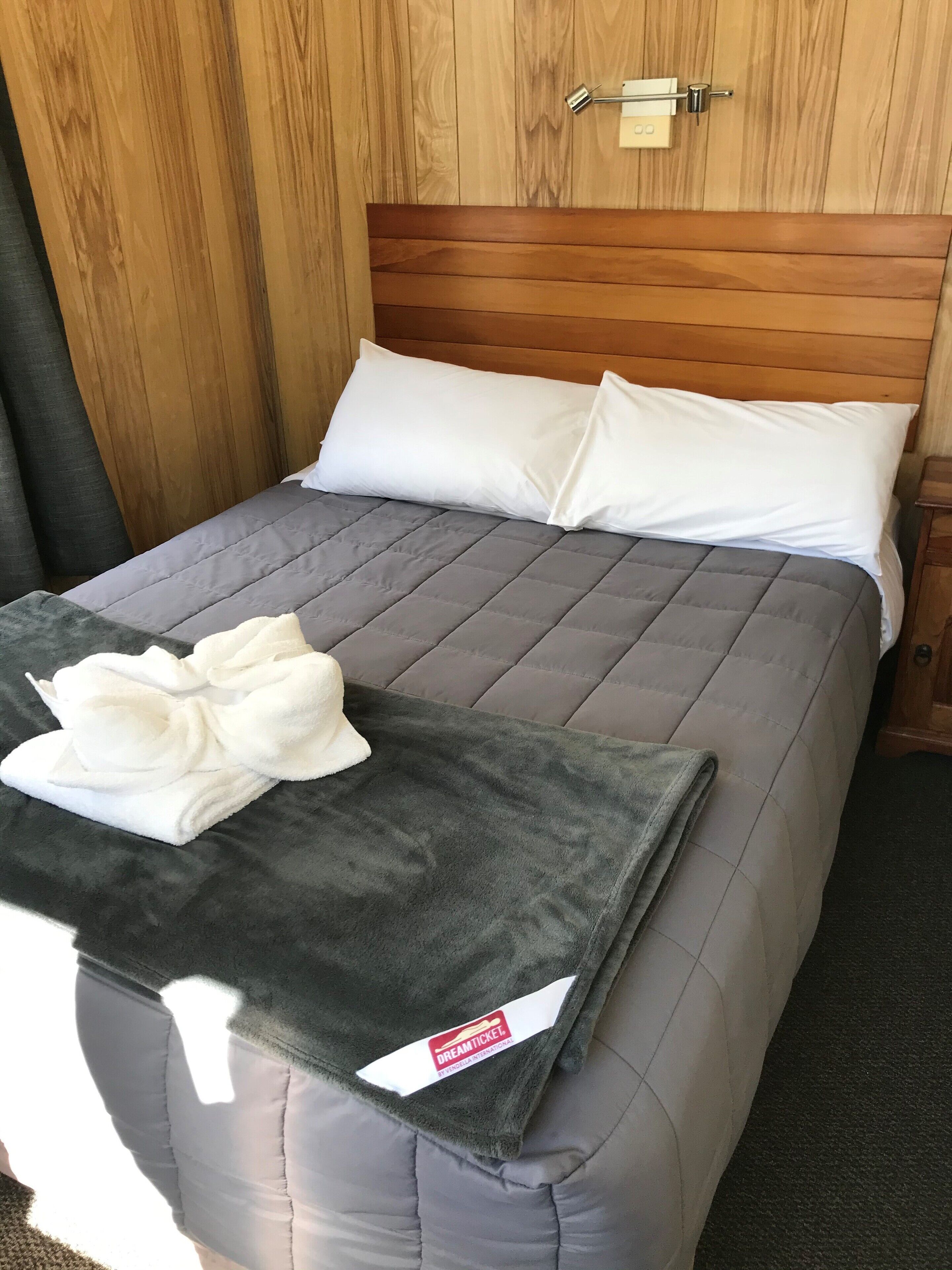 Un lit bien fait, avec une couverture grise, des oreillers blancs et une serviette blanche pliée posée sur un plaid gris.