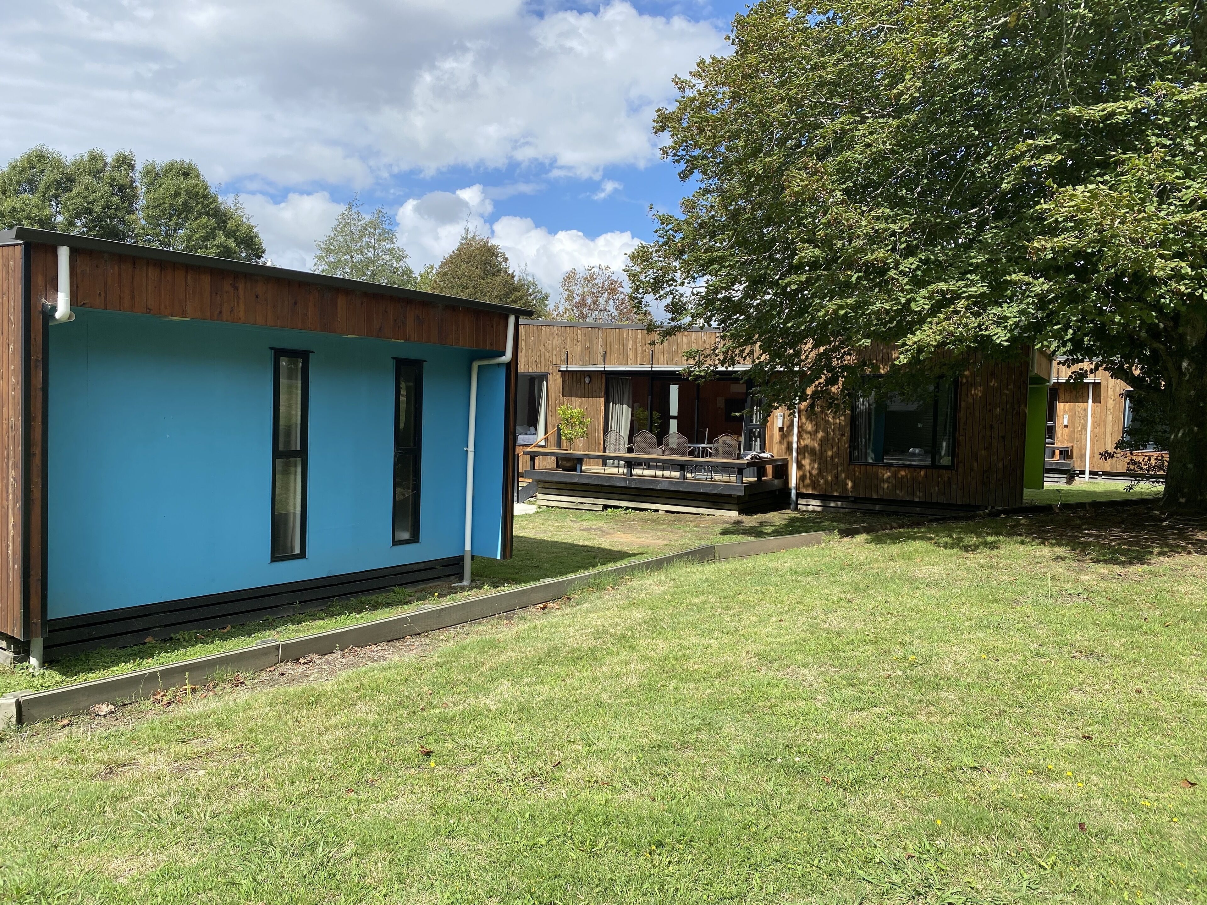 A modern building with a blue exterior, a wooden deck, and a grassy yard.