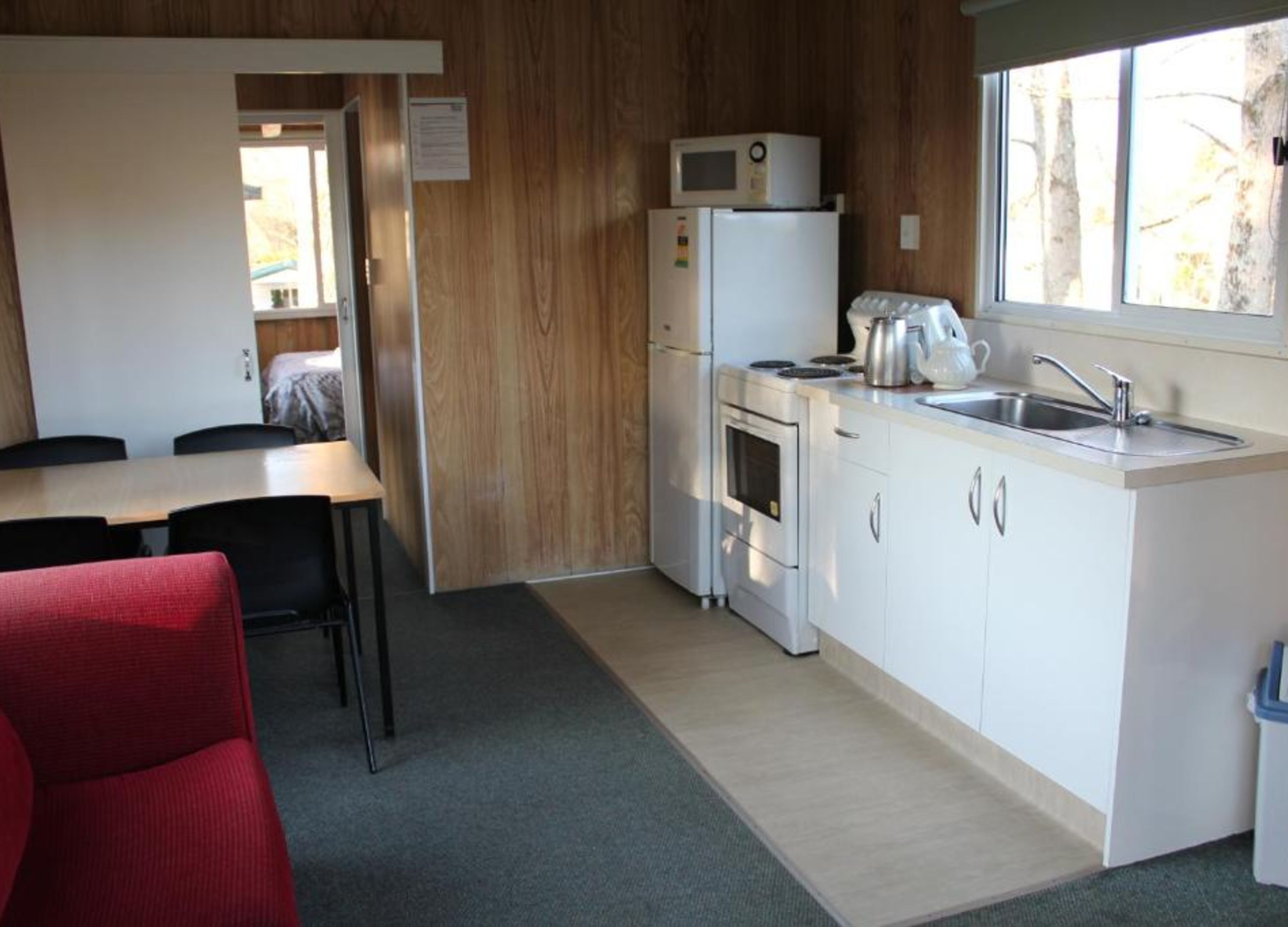 Een kleine keuken met een koelkast, magnetron, fornuis en een spoelbak. Er is een eethoek met een tafel en stoelen.