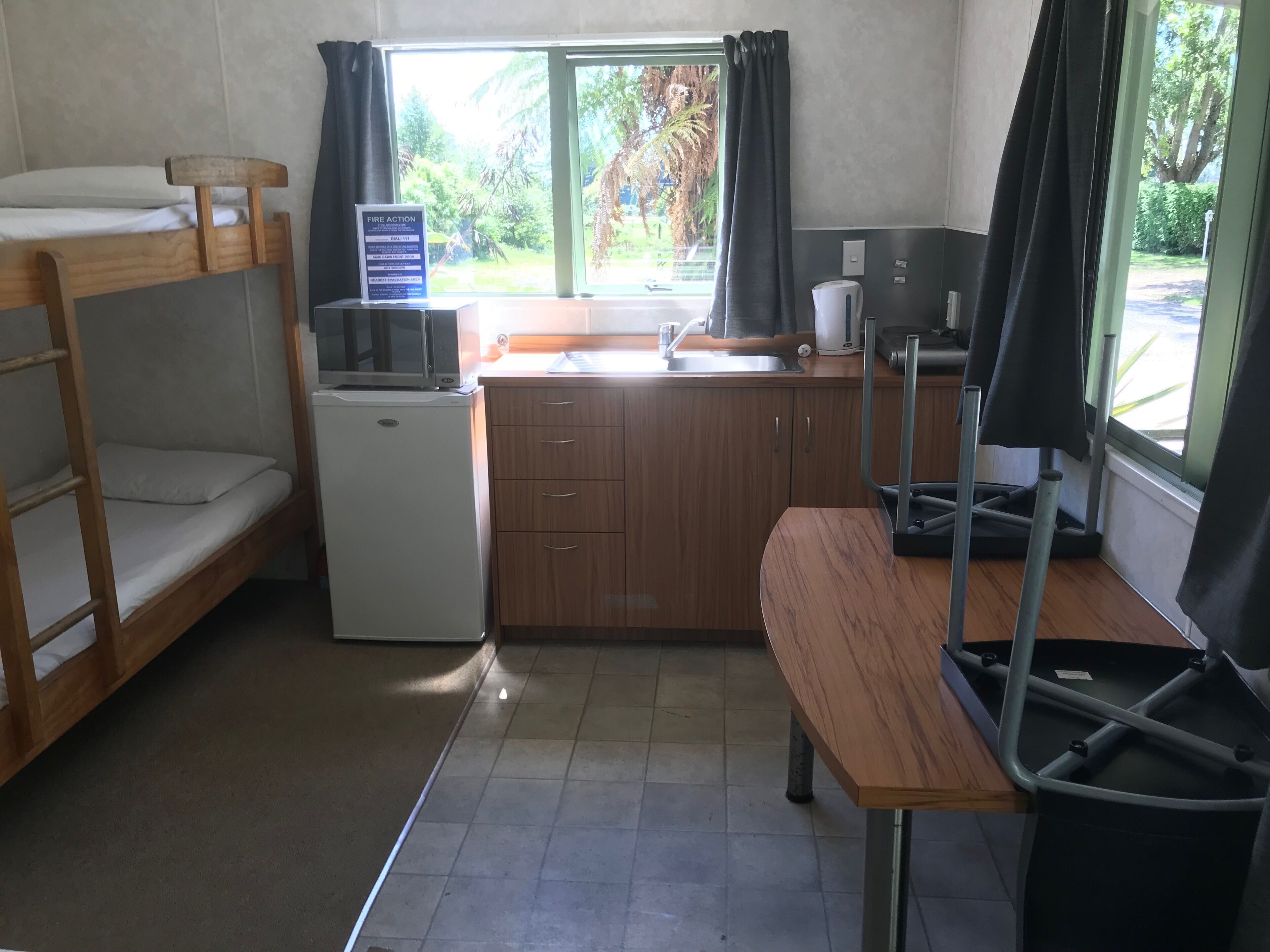 Habitación pequeña con literas, un rincón de cocina, un lavamanos y una ventana con cortinas.