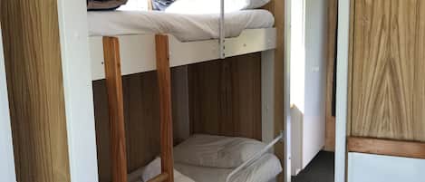 Ein Schlafraum mit Etagenbetten, Holzwandverkleidung und dunklem Boden.