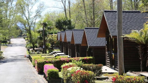 Una hilera de cabañas de madera con un sendero pavimentado que las conduce, rodeadas de jardines cuidados y árboles.