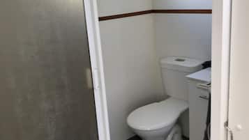A small, compact bathroom with a white toilet, a small window above it, and a wooden trim along the lower wall.