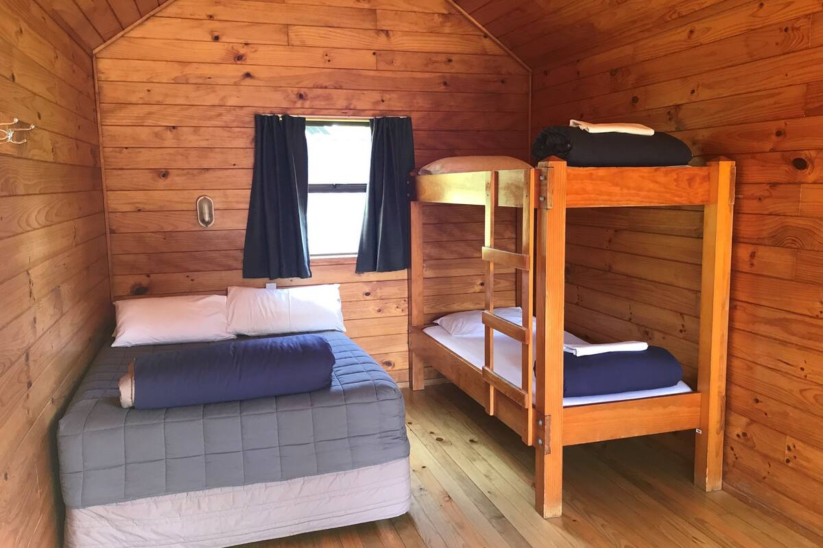 Une chambre dans un chalet en bois, avec un lit superposé et un lit simple.