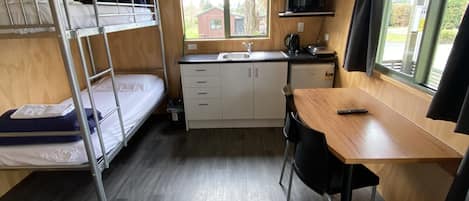 Ein kleines Zimmer mit Etagenbetten, einer Küchenzeile, einem Esstisch und einem Fenster mit Außenblick.